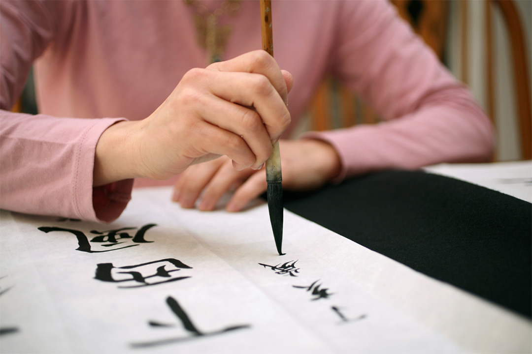 A person's hand painting calligraphy characters with a brush